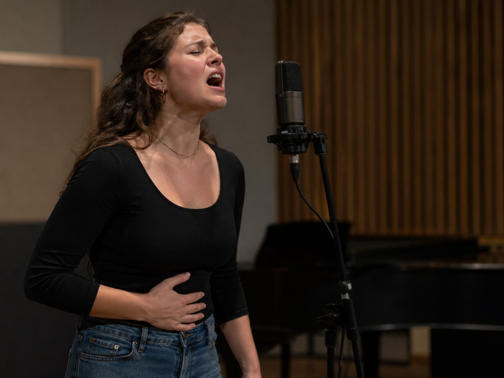 Une chanteuse tente une note difficile en plaçant la main sur son ventre, comme si elle cherchait à “soutenir” davantage : une image claire des malentendus fréquents autour de chanter aigu sans forcer.